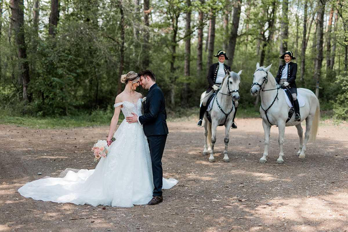 Brautpaar im Wald mit Pferden und Reitern im Hintergrund